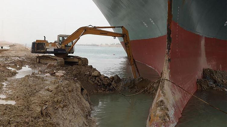 Picture of teeny tiny excavator doing its best to drag sand away from the hull of the boat